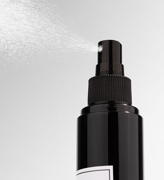 Black spray bottle with mist being released on a light gray background
