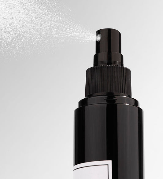 Black spray bottle with mist being released on a light gray background