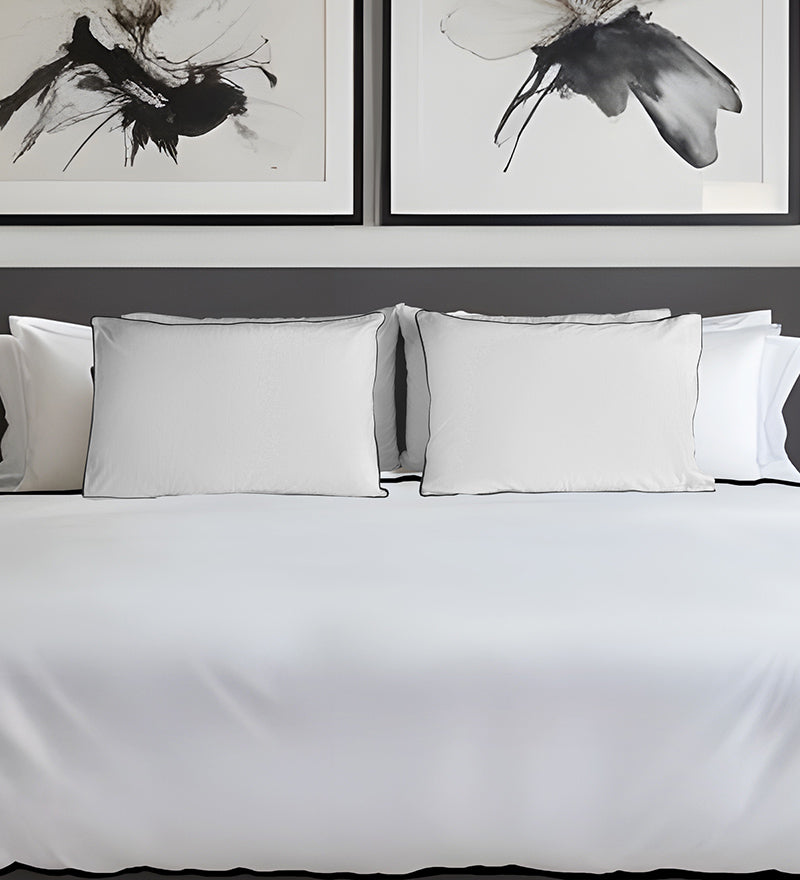 White bedding set with pillows on a bed, framed black and white artworks on the wall.