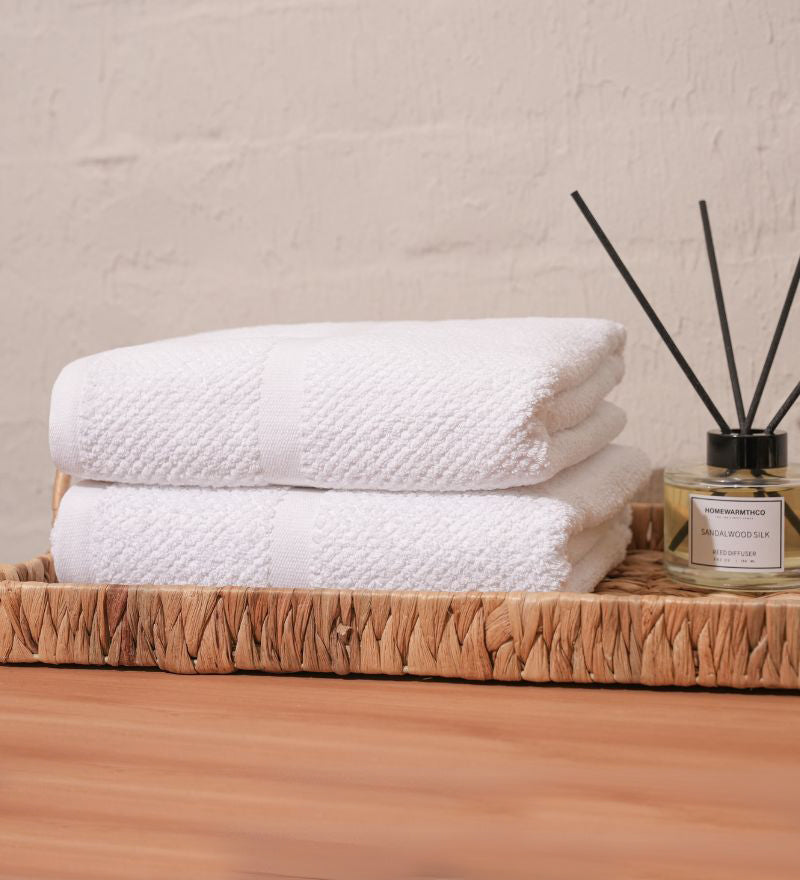 Stack of white towels on a wooden tray with a diffuser bottle in the background.