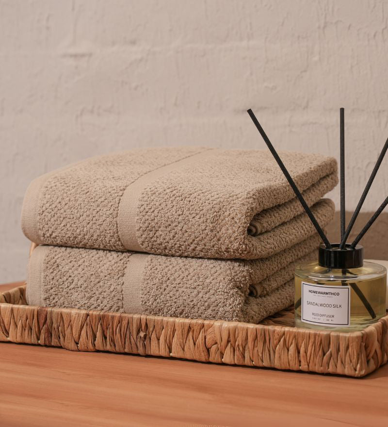 Stack of beige towels on a wooden tray with a diffuser bottle in the background.