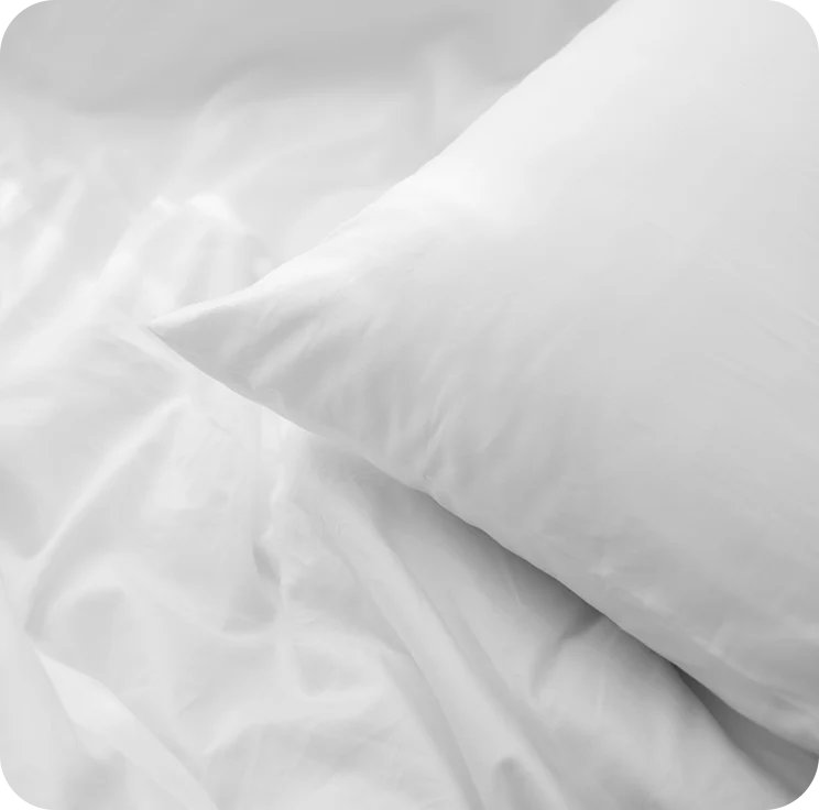 Close-up of white bedding with a pillow on a light gray background