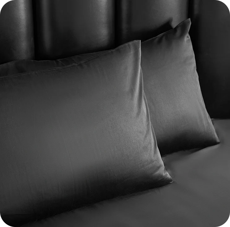 Two dark gray pillows on a bed with a black headboard.
