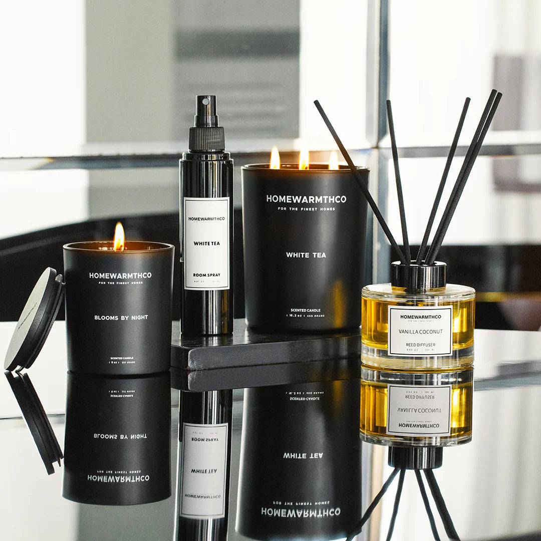 Collection of HomeWarmthCo candles, diffusers and room spray on a reflective surface.