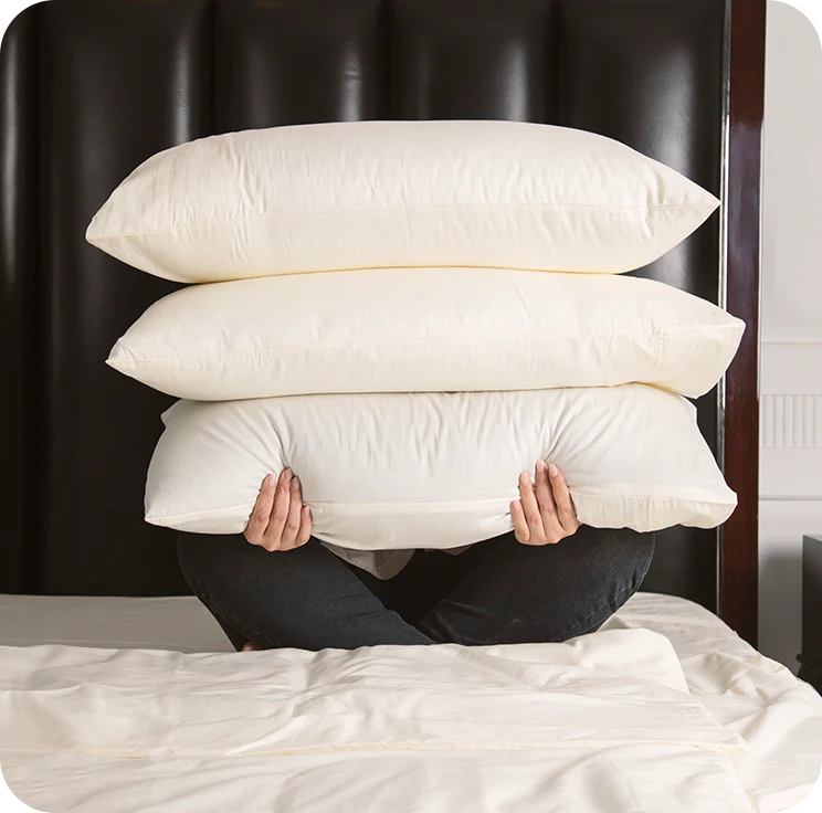 Person holding three pillows under a bed with a dark headboard.