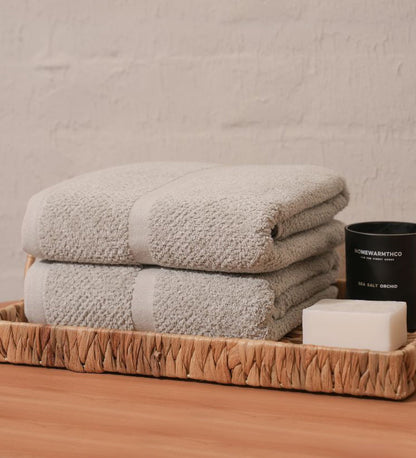Stack of folded towels on a woven tray with a candle and soap bar against a neutral background