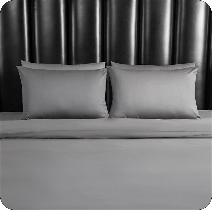 Gray bedding set with pillows on a bed against a dark headboard.