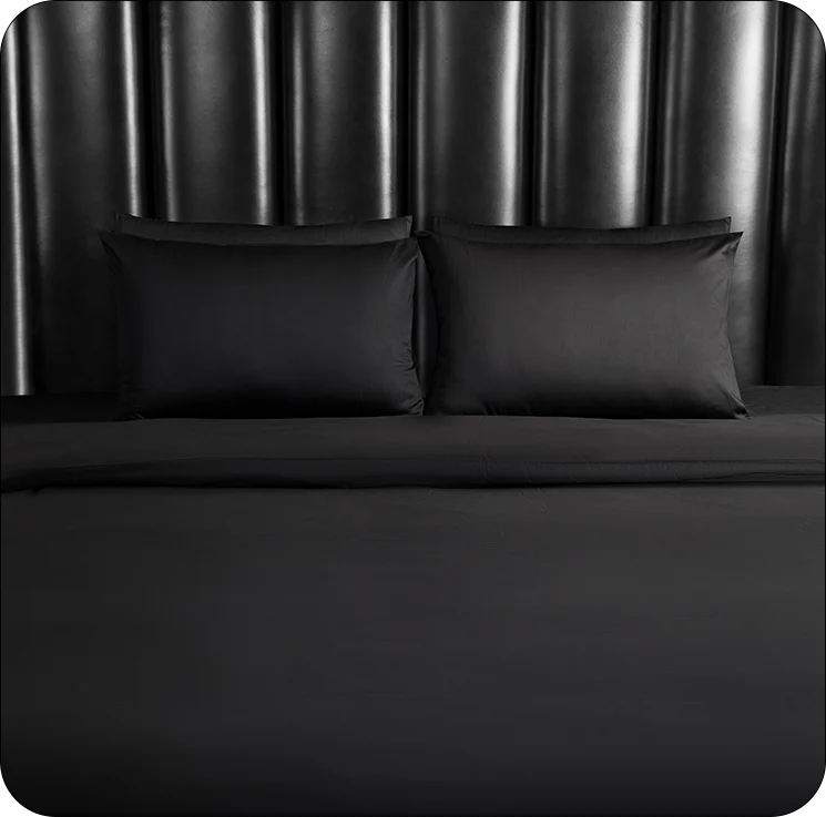 Black bedding set with pillows on a bed against a dark headboard.