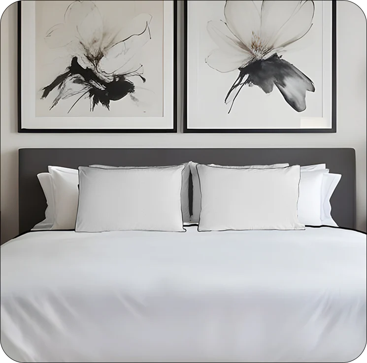Bedroom with white bedding, gray headboard, and black and white floral artworks on the wall.