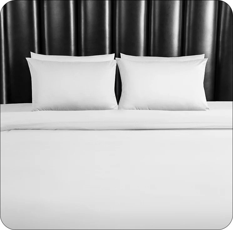 White bedding set with two pillows on a bed against a dark headboard.