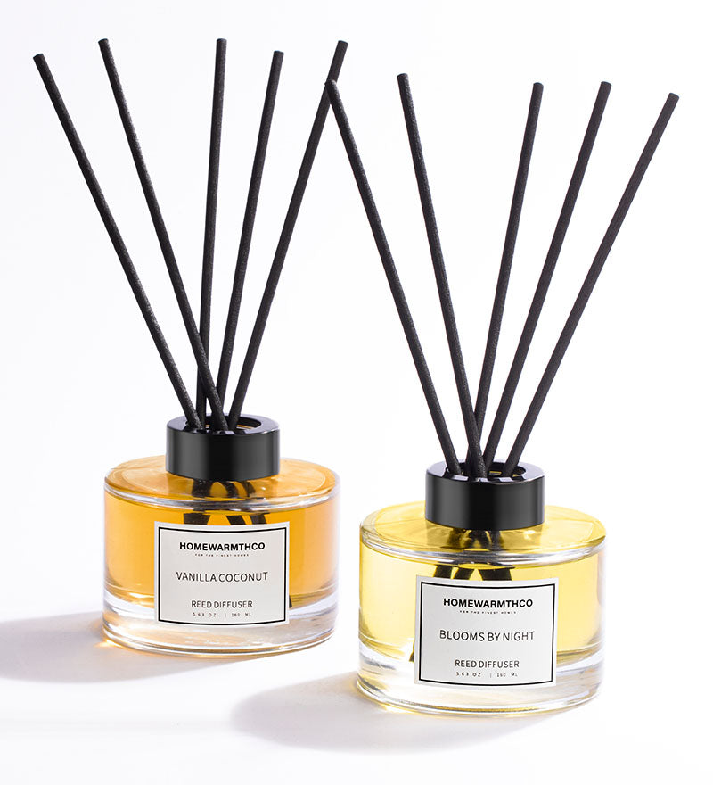 Two Homewarmthco reed diffusers with black sticks on a white background