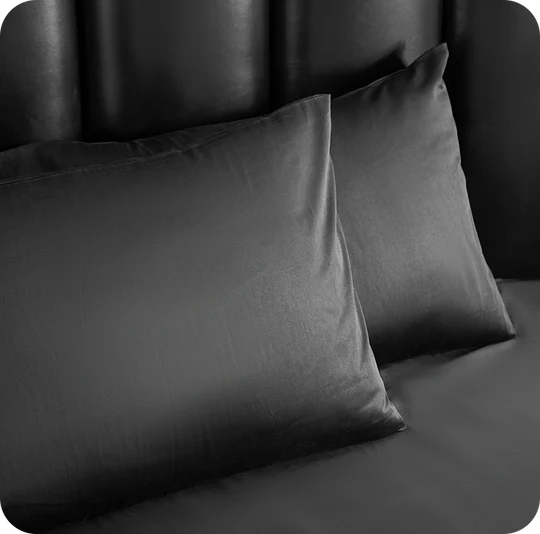 Two dark gray pillows on a bed with a black headboard.