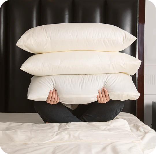 Person holding a stack of pillows on a bed