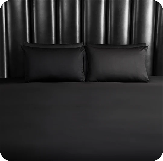 Black bed sheets and pillows on a bed with a dark curtain background