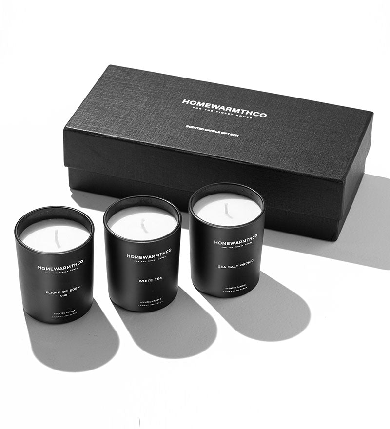 Three black candles with white lids on a gray surface, with a black box labeled 'Homewarmth Co' in the background.
