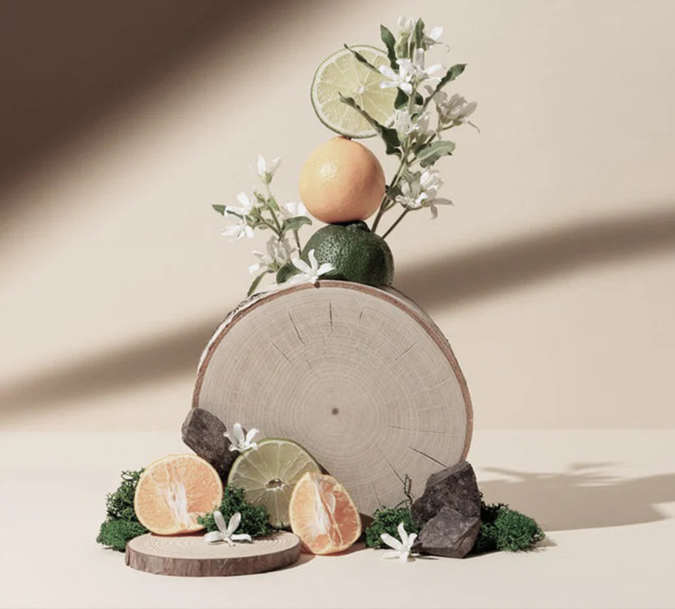 reed diffuser Decorative arrangement with citrus fruits and flowers on a wooden log against a neutral background