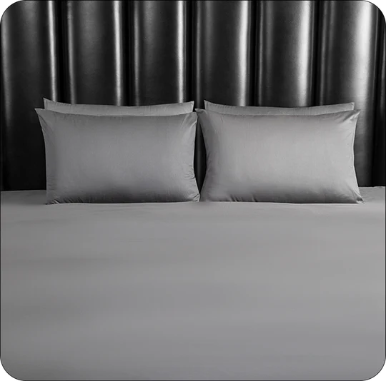 Gray bedding set with two pillows on a bed against a dark headboard.