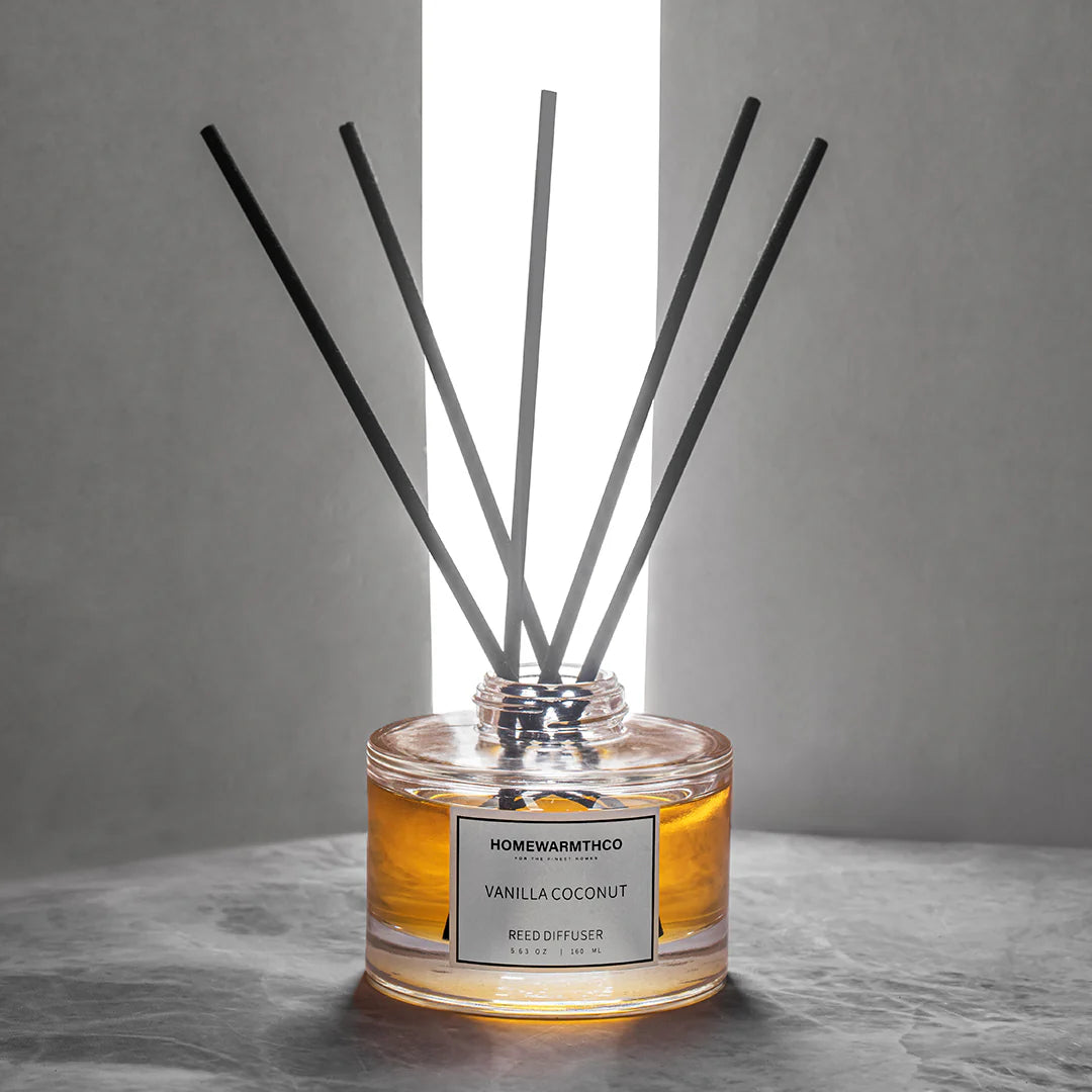 Reed diffuser with black sticks in a clear jar on a gray surface