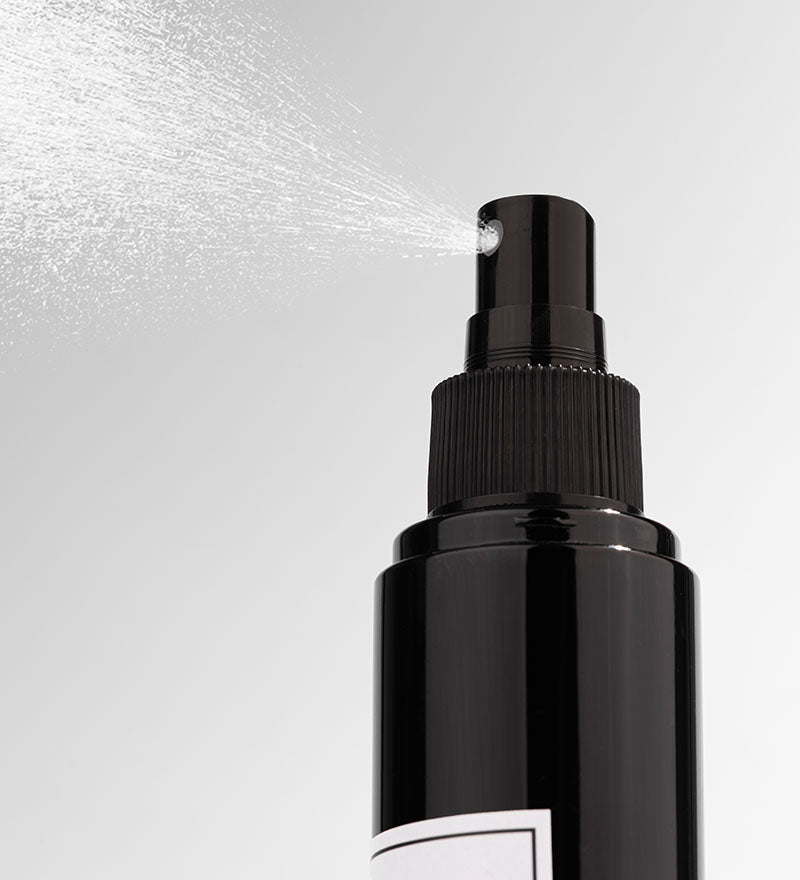 Black spray bottle with mist being released on a light gray background
