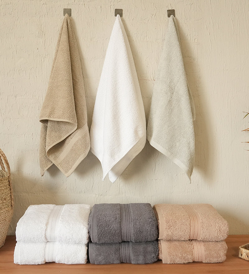 Set of folded and hanging towels on a wooden surface with a neutral wall background.