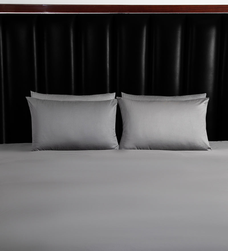 Gray bedding set with two pillows on a bed against a black headboard.