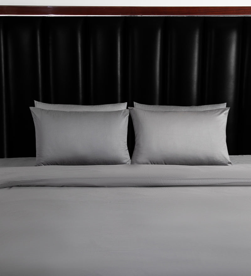 Gray bedding set with two pillows on a bed against a black headboard.