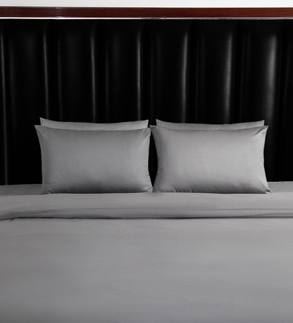 Gray bedding set with two pillows on a bed against a black headboard.