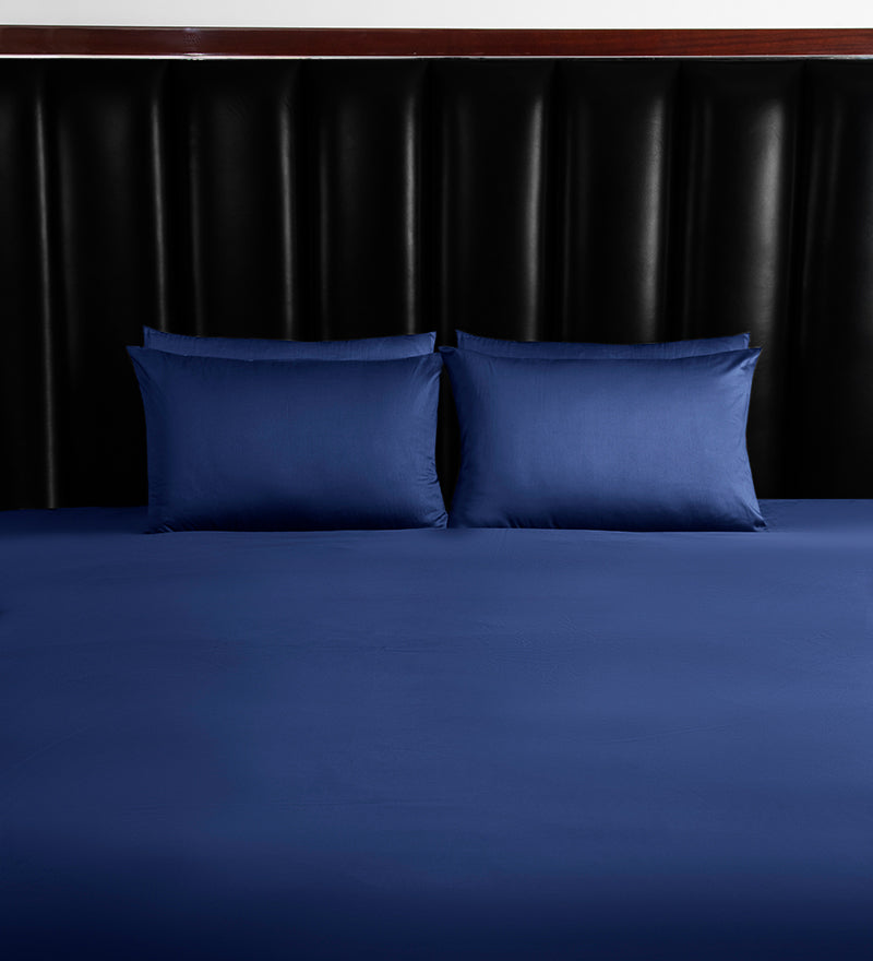 Two blue pillows on a bed with a dark headboard