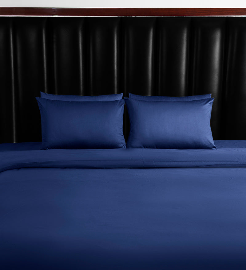 Blue bed sheets and pillows on a bed with a dark headboard.