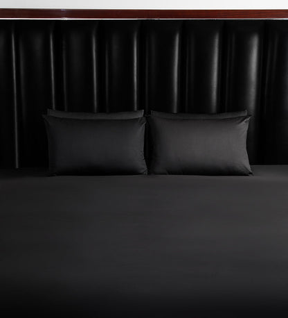 Two black pillows on a bed with a dark headboard