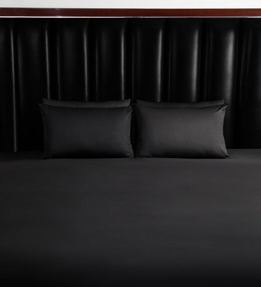 Two black pillows on a bed with a dark headboard