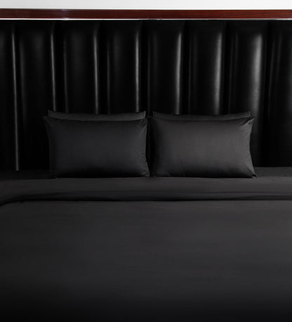 Dark grey bedsheets are set on a bed with a black headboard.