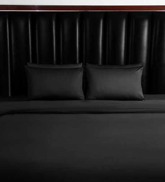Dark grey bedsheets are set on a bed with a black headboard.
