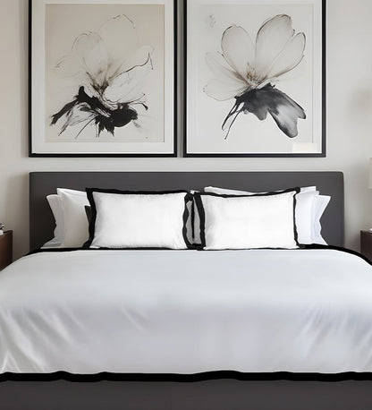 Bedroom with a bed featuring white bedding and black headboard, framed floral artworks on the wall.