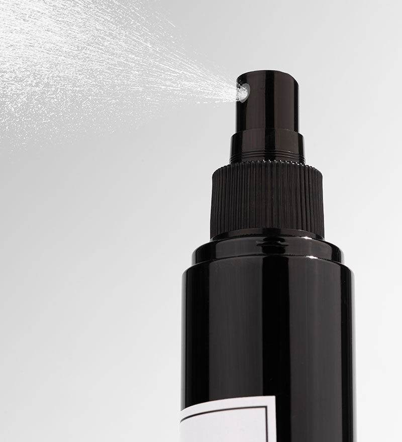 Black spray bottle with mist being released on a light gray background