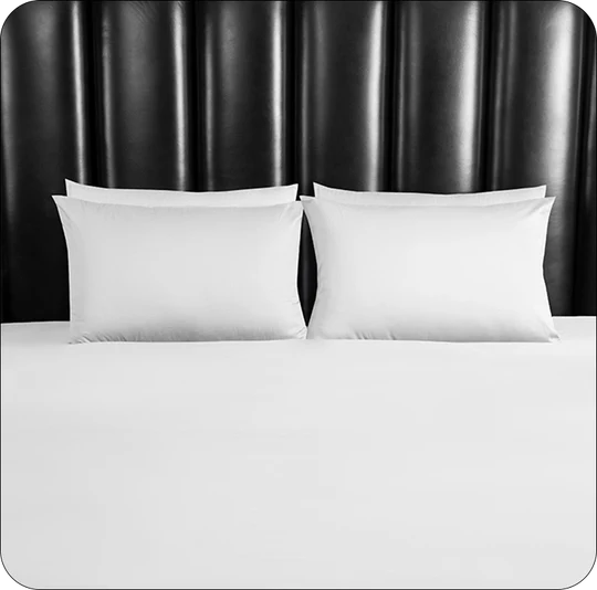 White bedding set with two pillows on a bed against a black headboard.